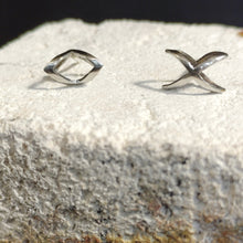 Load image into Gallery viewer, Stainless Steel earrings one X and one O with sterling silver ear posts and silicone earring backs. The jewelry is set on a white stone with a black background. Outwitting injustice with love for humanity.